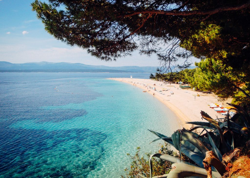 Strand mit türkisfarbenem Wasser und Kieselsteinen, umgeben von Pinien, Dalmatien