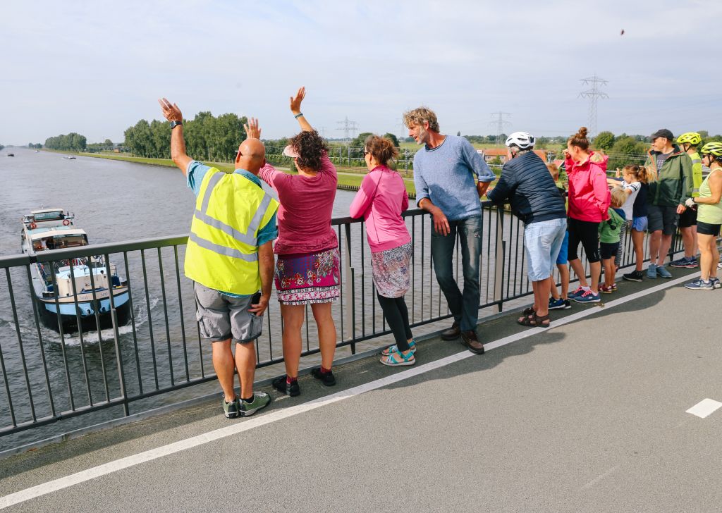 Group of tourists greet the people on the boat sailing on the canal from the bridge