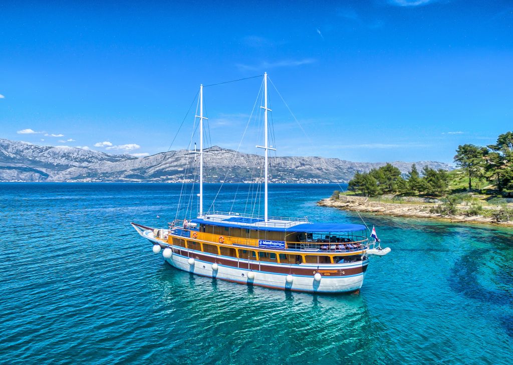 Barca a vela ancorata vicino a un'isola verdeggiante lungo la costa della Croazia.