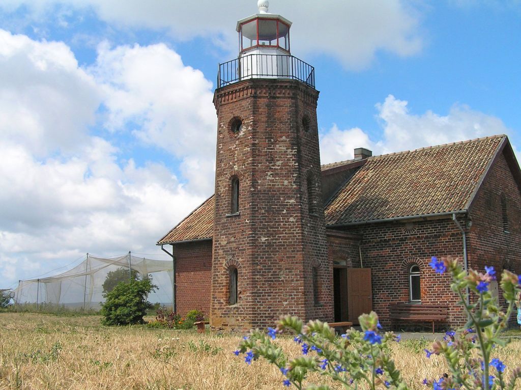 Faro storico di Nida, Penisola dei Curi, Lituania, circondato da cielo azzurro e vegetazione.