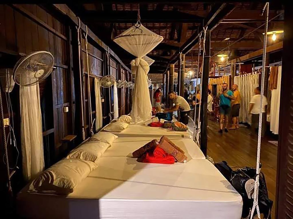 Corridoio serale con letti e zanzariere in lodge su palafitte, atmosfera conviviale del tour culturale in Cambogia