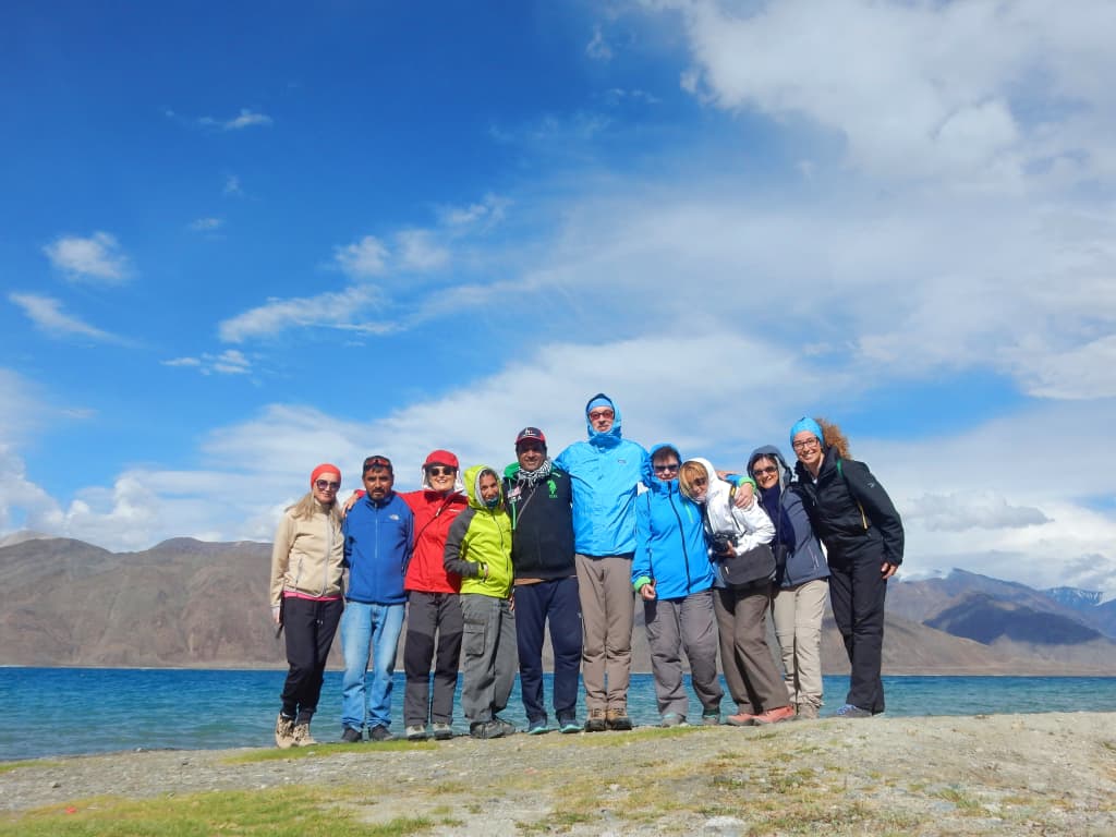 Gruppo di trekker sulle rive del lago Pangong Tso, Ladakh: acque turchesi e vette himalayane sullo sfondo.