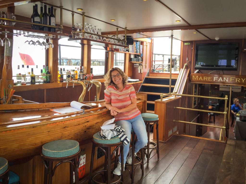 Interno di una nave a vela con un ospite sorridente seduta al tavolo, Isole Frisone