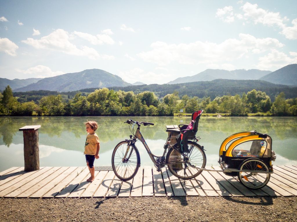 Bambino vicino a una bici su un pontile lungo il fiume, ciclabile della drava, famiglia in viaggio con bici "Girolibero", vacanze in bici e barca