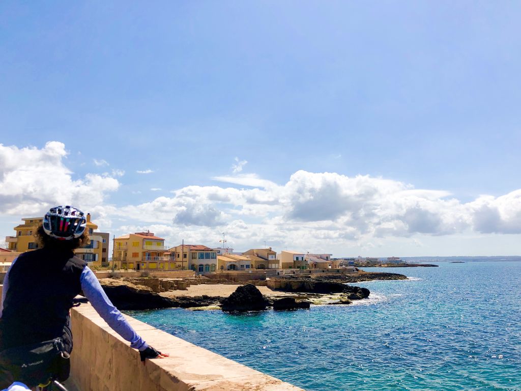 Ciclista ferma al ammirare un villaggio, mare cristallino con scogliere e insenature rocciose a Maiorca.