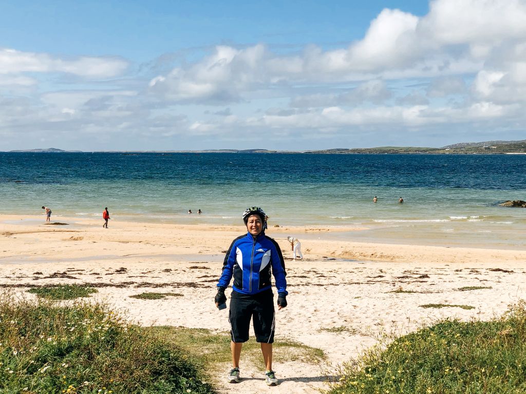 Uomo sulla spiaggia di sabbia bianca, con mare e cielo sereni nel Connemara.