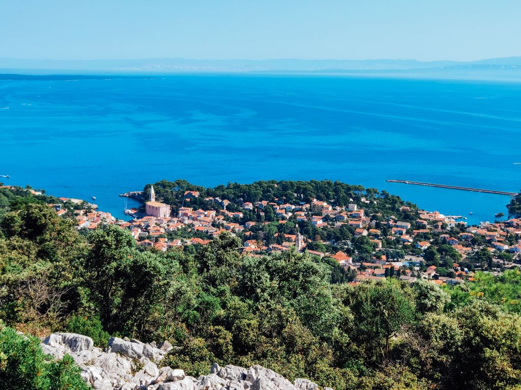 Küstenweg mit Blick auf ein Dorf zwischen Vegetation und Meer, Kroatien