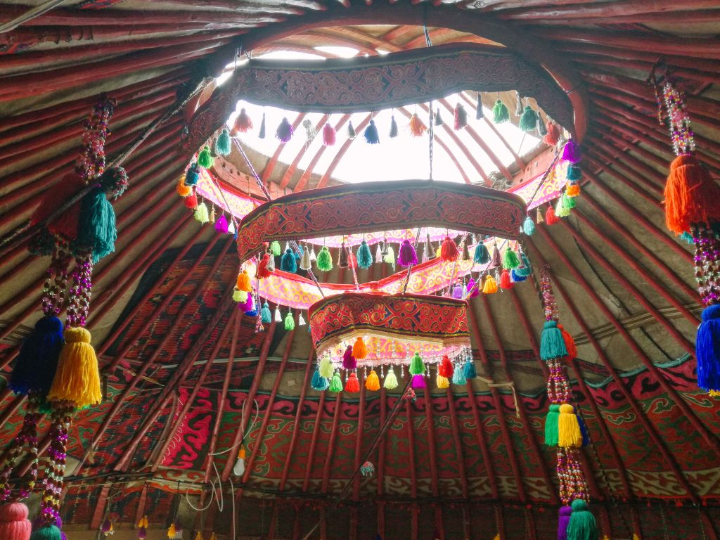Interno di una yurta decorata con motivi colorati tradizionali kirghisi, illuminata dalla luce naturale.