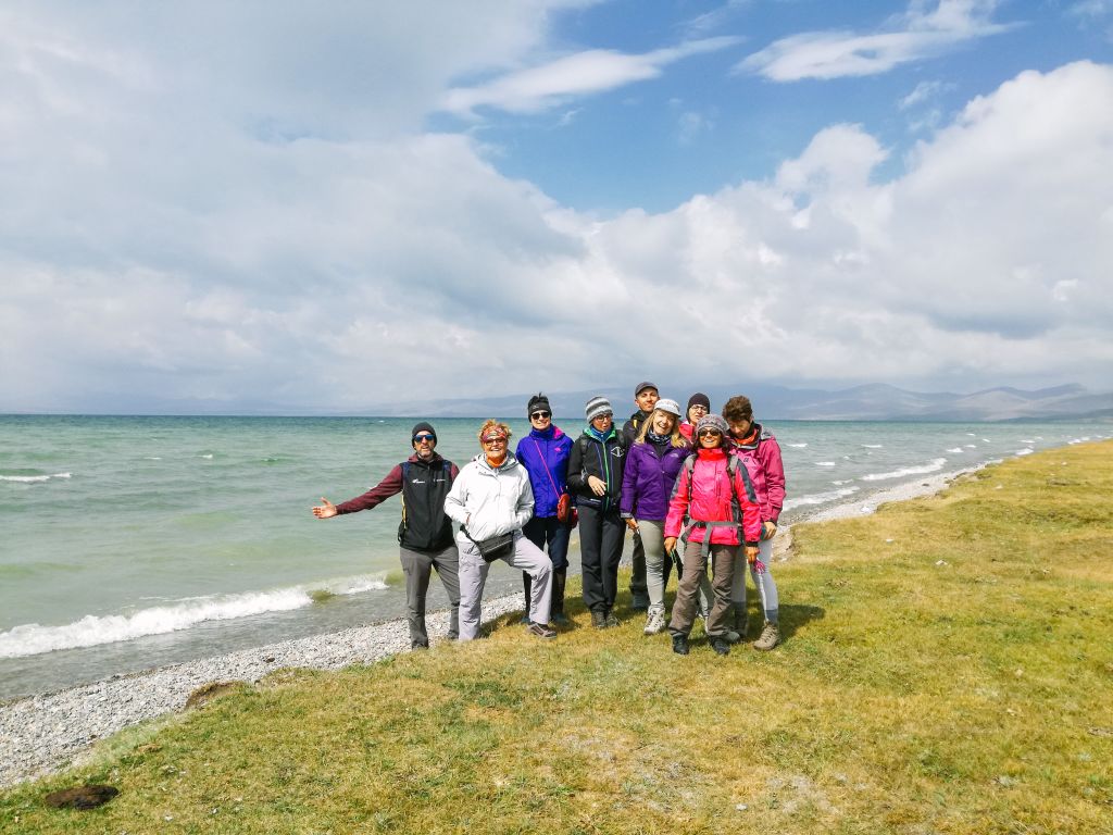 Turisti in posa vicino al lago Song Kol con cielo limpido e acqua cristallina in Kirghizistan.
