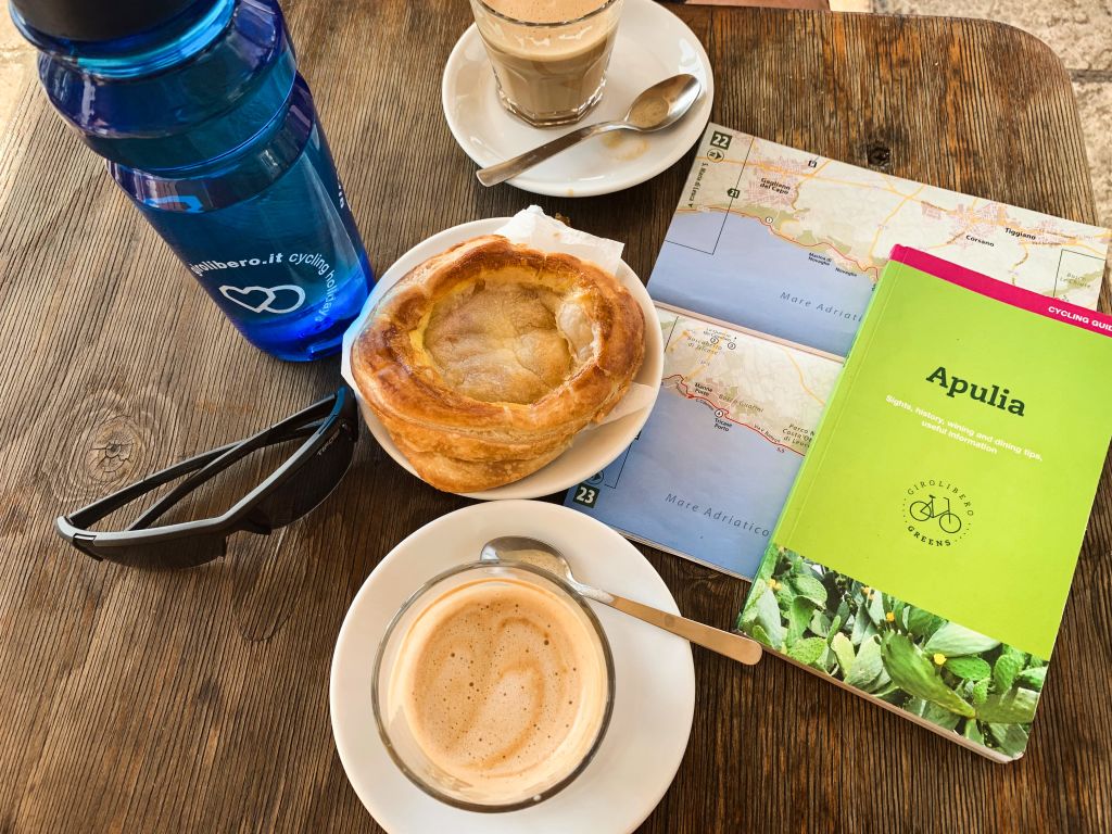 Colazione con cappuccino e dolci in un bar, mappa percorsi e borraccia, viaggio cicloturistico in Puglia, Salento