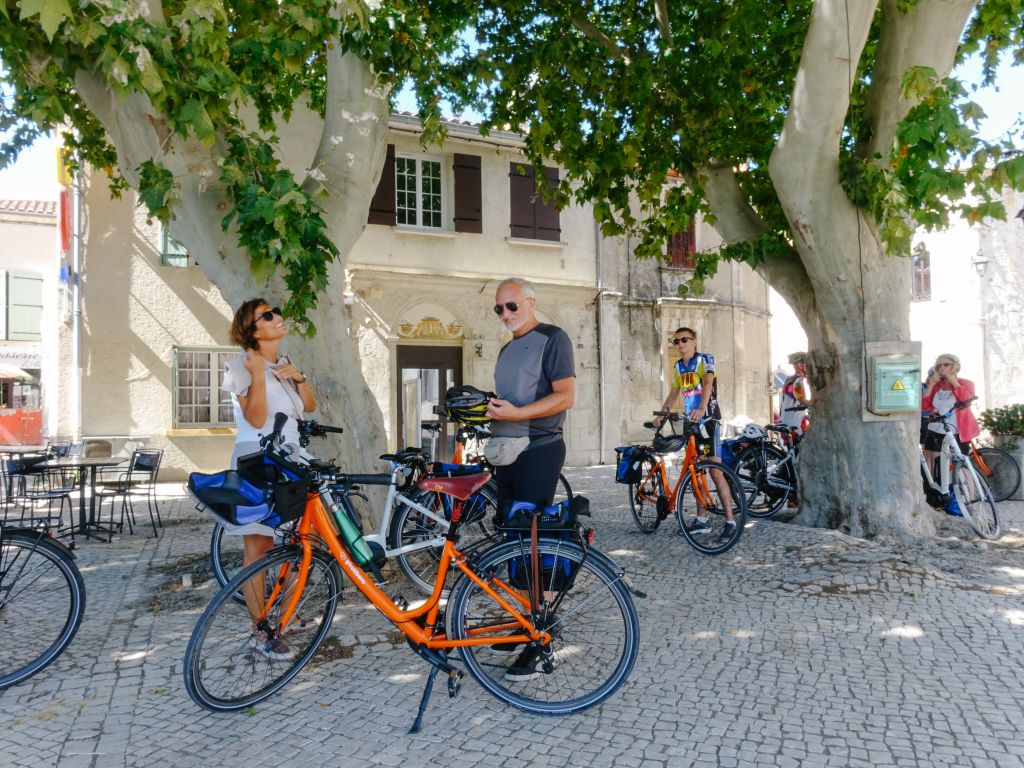 Biciclette arancioni di Girolibero parcheggiate in una piazza alberata, viaggi in bici Provenza e Camargue