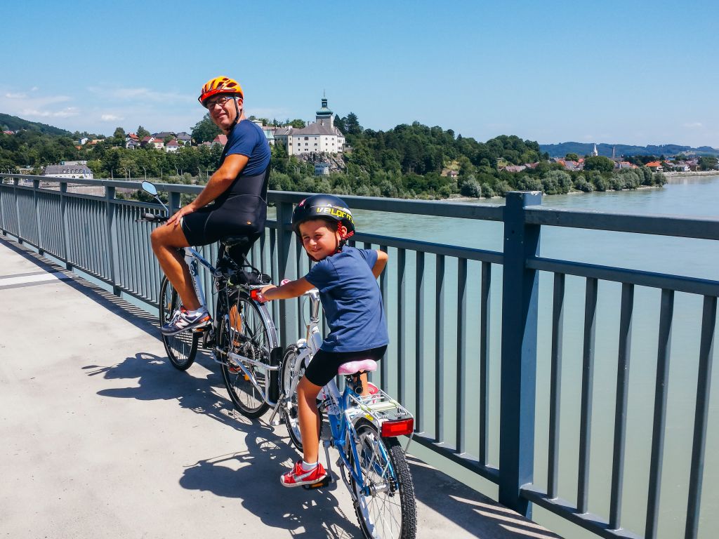 Papà con bambino in bici con caschetto, follow me tandem, lungo la ciclabile del fiume Danubio