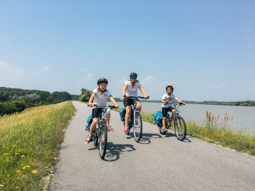 Famiglia con bambini in bici con caschetto, fiume Danubio, paesaggio verde, vacanza all&#39;aria aperta, Austria