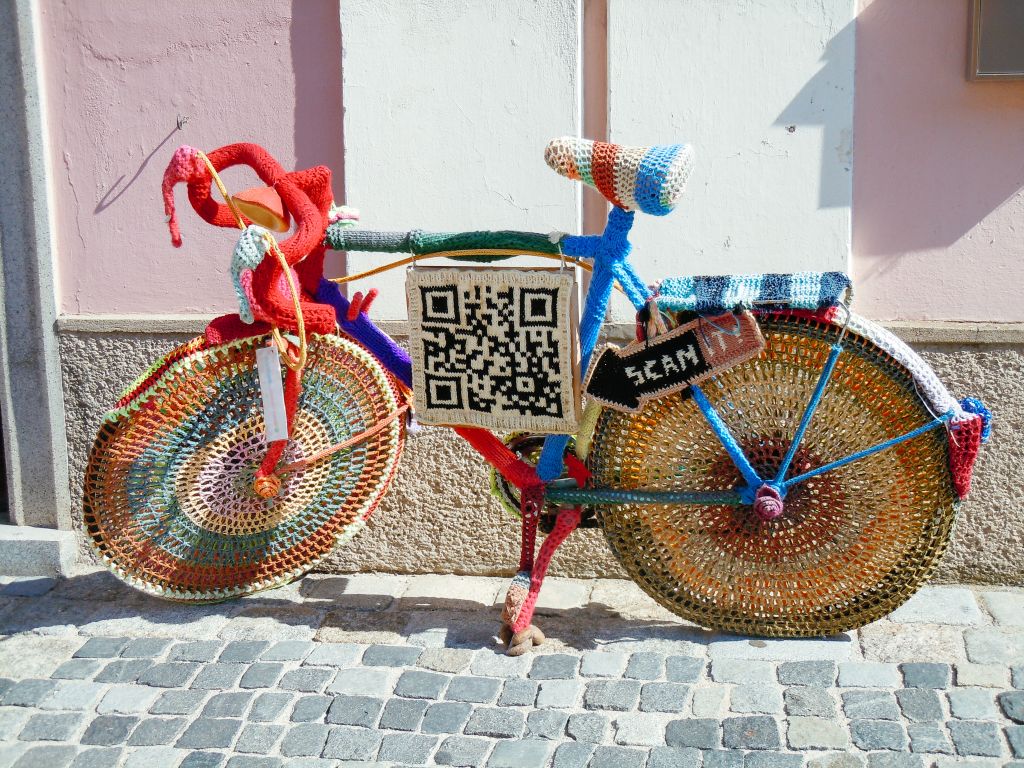 Bici decorativa coperta di lana intrecciata con indicazione di un QR code da scannerizzare, tra Austria e Germania
