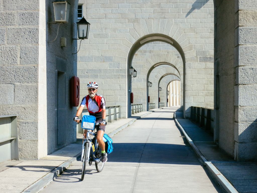 Cicloturista con caschetto, passaggio bici e pedonale ad archi grigi, Passau Vienna, tra Germania e Austria