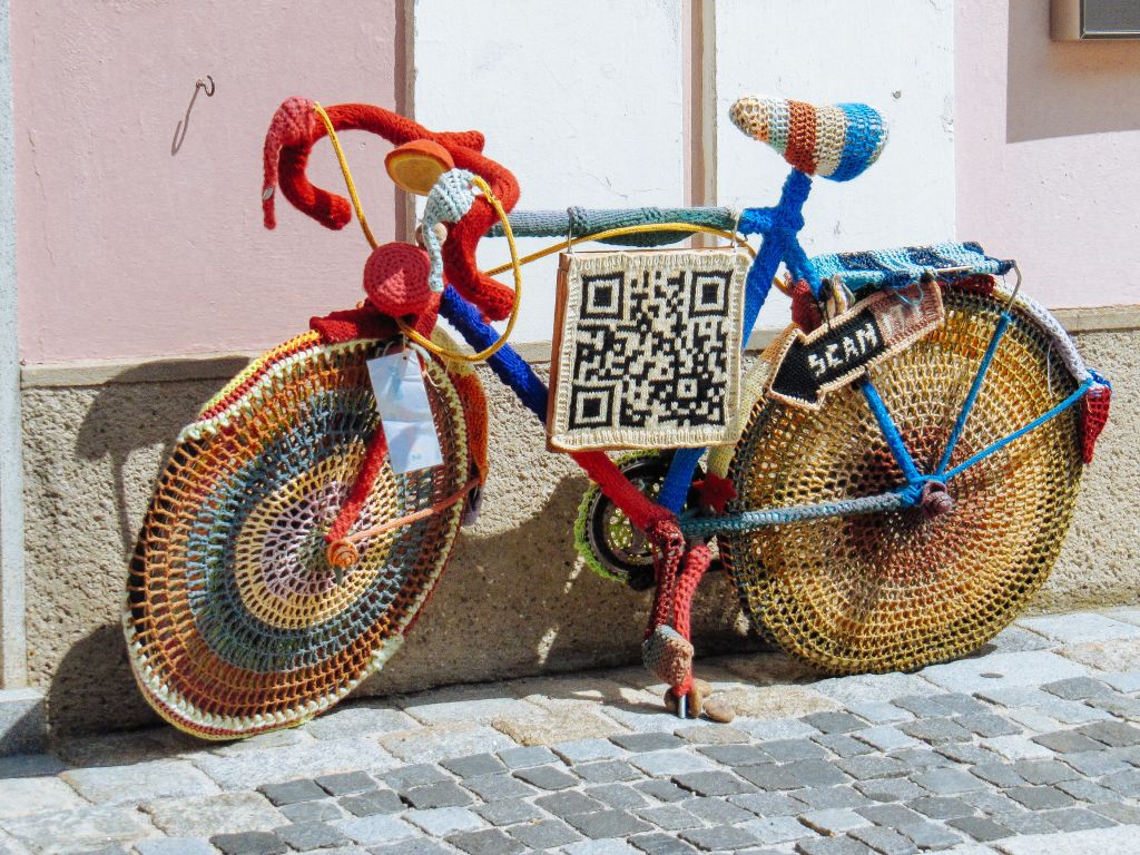 Bici decorativa coperta di lana intrecciata con indicazione di un QR code da scannerizzare, tra Austria e Germania