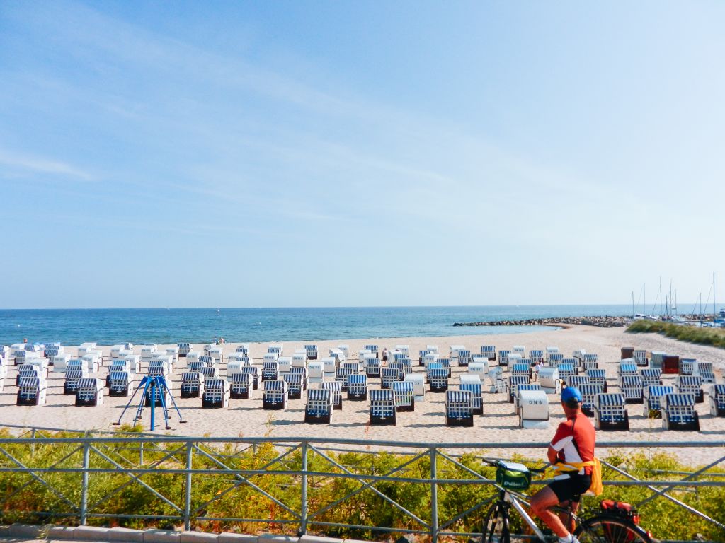 Ciclista osserva una spiaggia con cabine colorate, ciclabile lungo il Mar Baltico.