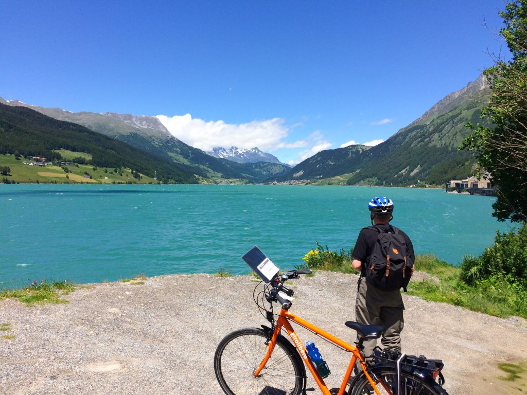 Cicloturista di spalle, bici muscolare Girolibero, paesaggio lacustre, montagne verdi, lago, Trentino Alto Adige