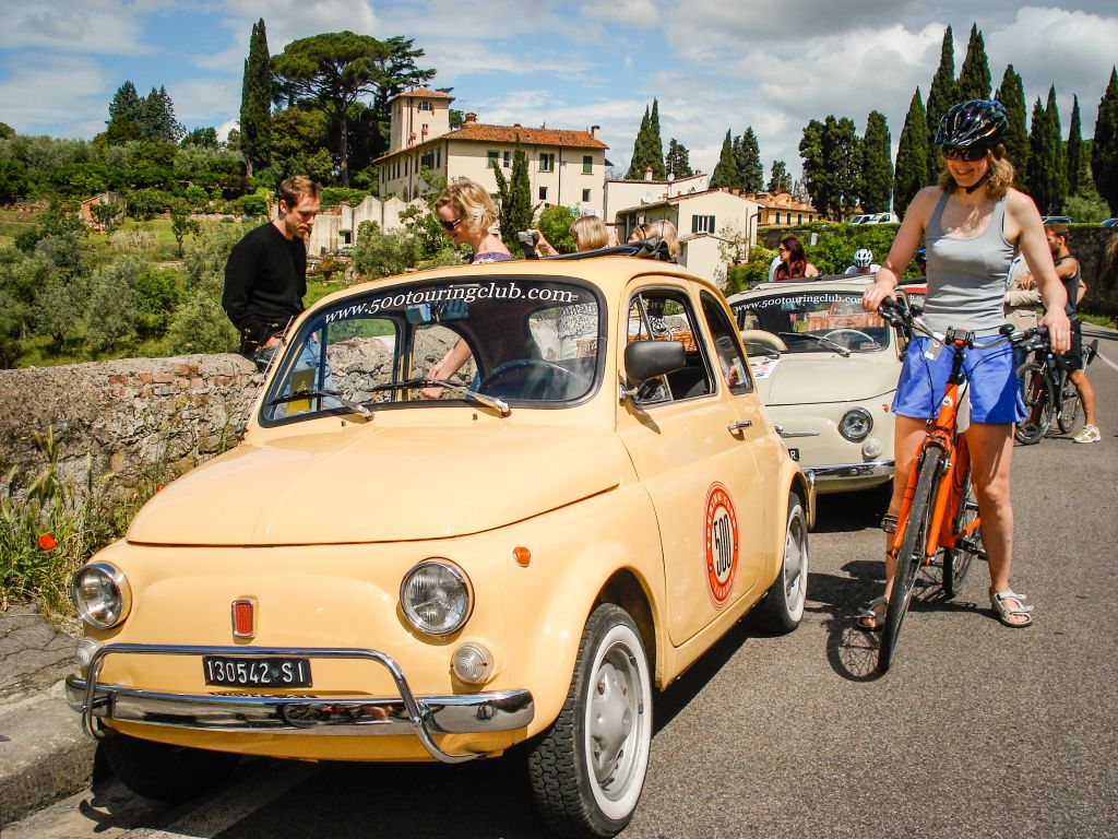 Familie mit Fahrrädern neben einem Vintage-Fiat 500 in den toskanischen Hügeln.