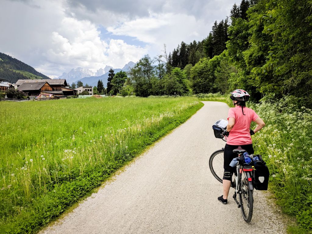 Cicloturista con caschetto ferma ad osservare il paesaggio, paesino di montagna, prato verde, tra Bolzano e Cortina