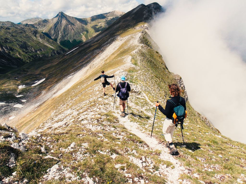 Camminatori con bastoncini da trekking percorrono un sentiero in cresta, Monti Sibillini, vacanze all'aria aperta, trekking di gruppo con guida Girolibero