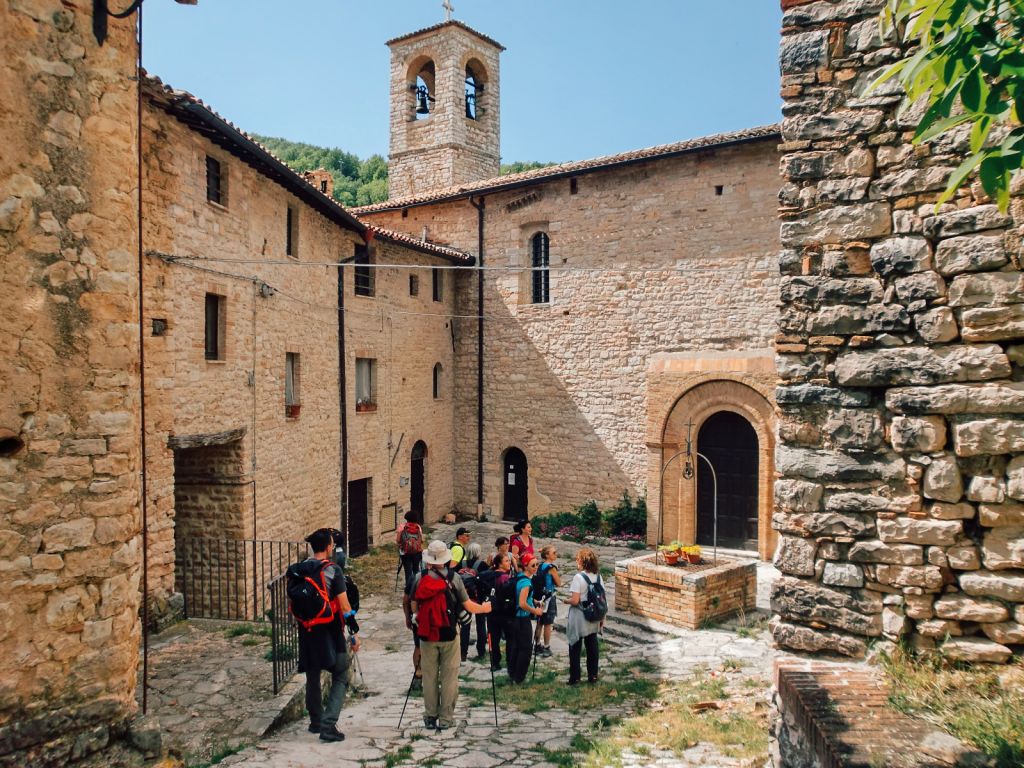 Escursionisti che attraversano un borgo storico in pietra, Castello di Croce, trekking dei Monti Sibillini, camminare in Italia.