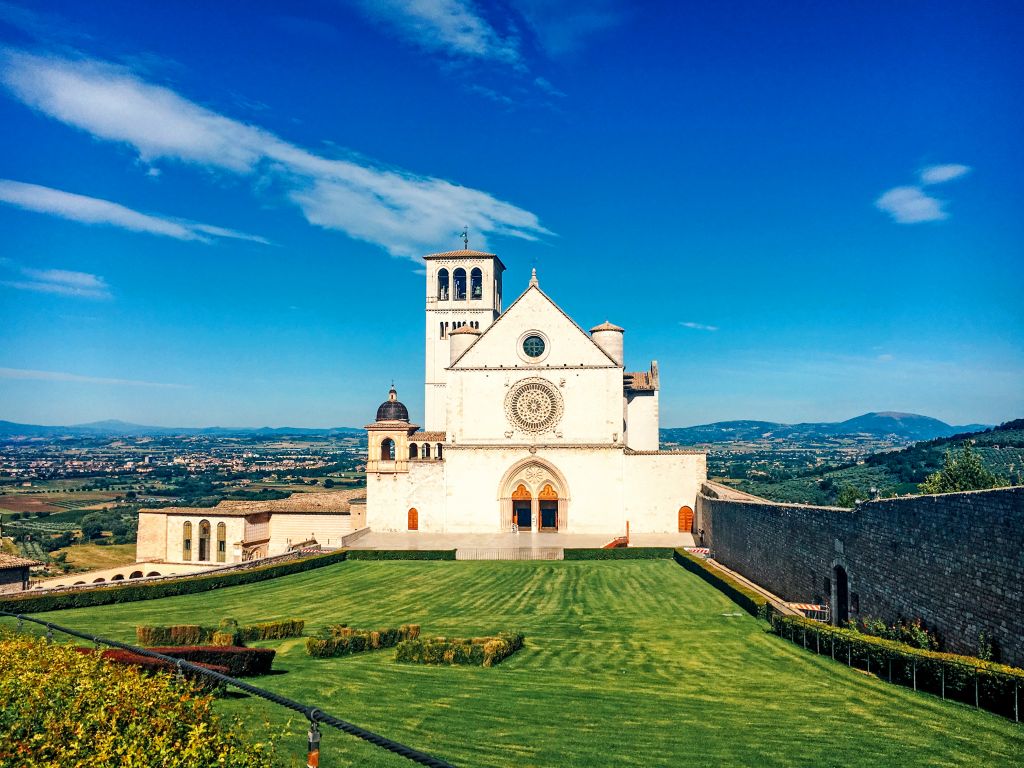 Facade of the Basilica of Saint Francis in Assisi with green lawn and blue sky.