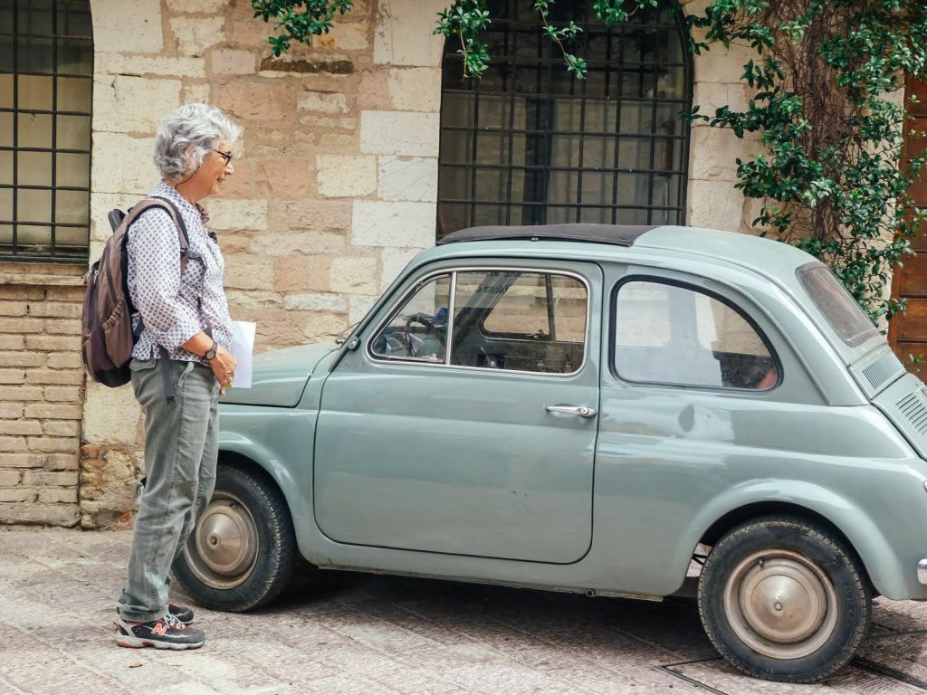 Persona davanti a una vecchia auto d'epoca Fiat 500 parcheggiata davanti a una casa in pietra, Umbria, Italia, via di San Francesco