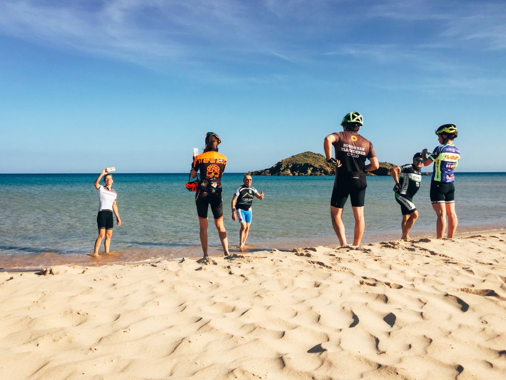 Gruppo di ciclisti in pausa per una foto su una spiaggia, tour in Sardegna.