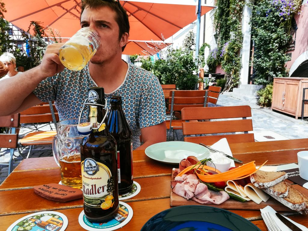Uomo che gusta una birra e piatti tipici bavaresi all’aperto in una birreria lungo la Romantische Strasse, Germania.