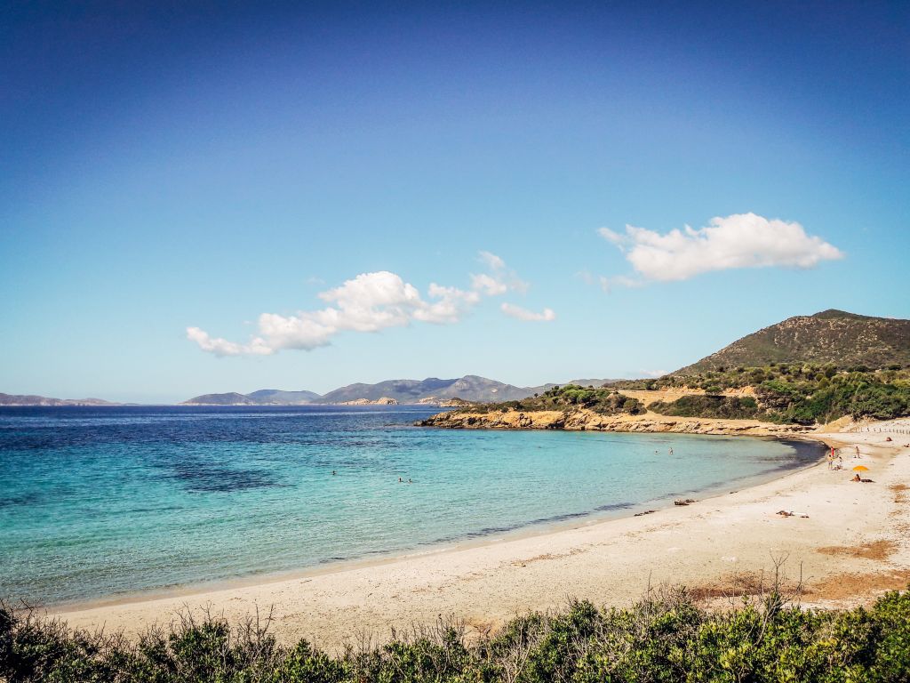 Spiaggia sabbiosa con acqua cristallina e colline sullo sfondo, Sardegna, il Sud-Ovest selvaggio