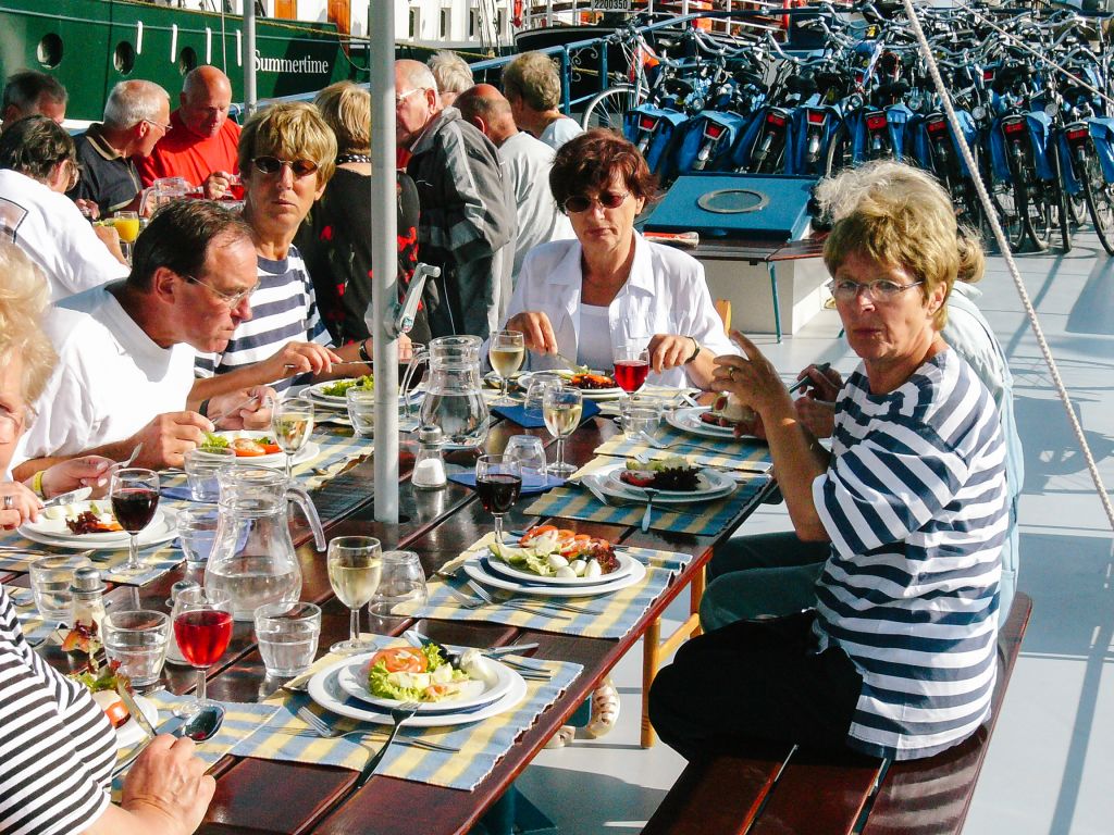 People having lunch on the deck of a tourist boat on a canal in Amsterdam with outdoor tables