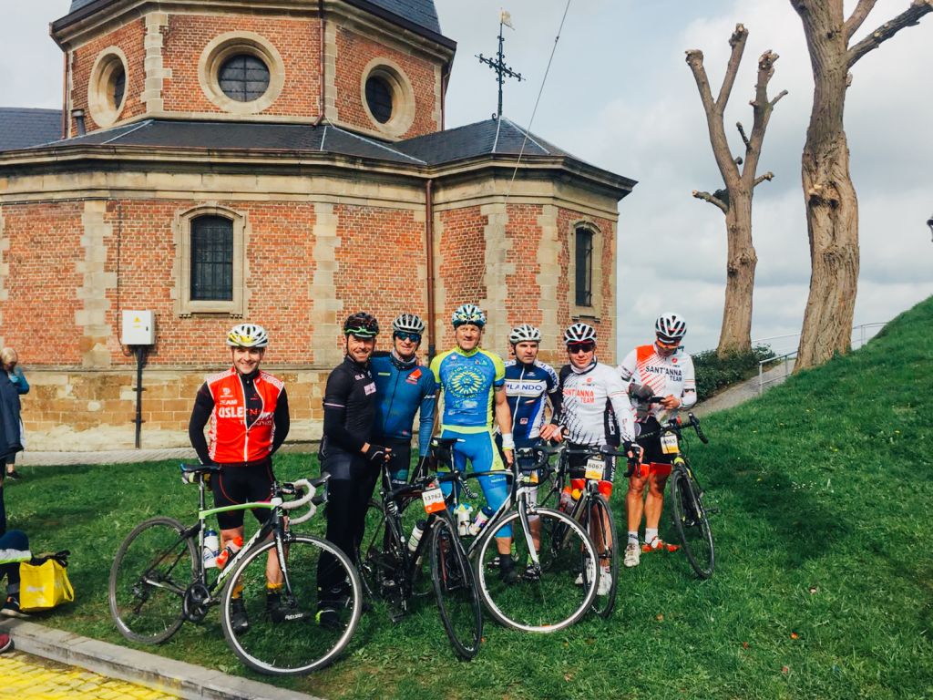Gruppo di ciclisti davanti a una chiesa storica in pietra, in una località rurale. Belgio, Francia bici da corsa