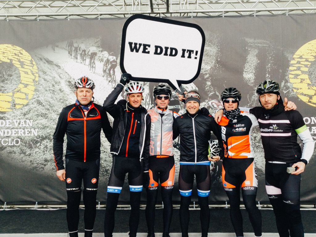 Gruppo di ciclisti che festeggiano con un cartello "We did it", evento ciclistico Fiandre