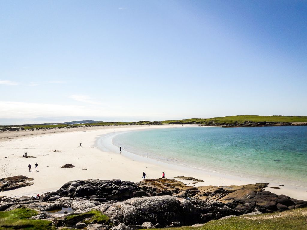 Spiaggia di sabbia bianca con bagnanti e rocce lungo la costa del Connemara.