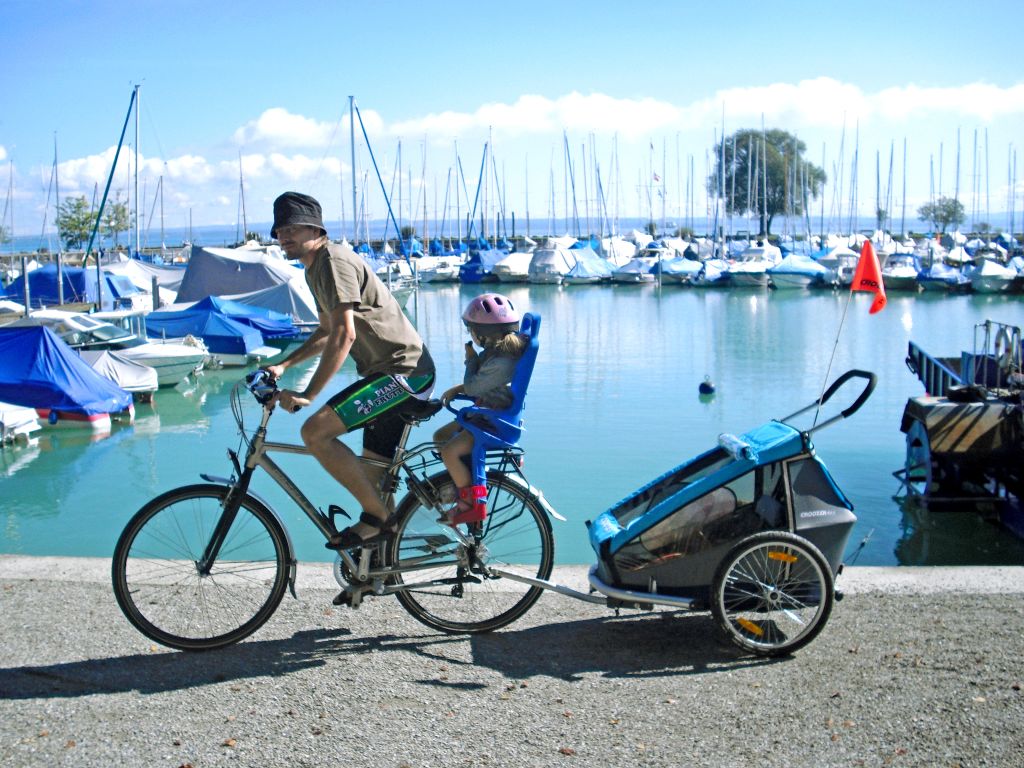Papà in bici con bambino con seggiolino e carretto sul molo, viaggi in bici per famiglie "Girolibero", Lago di Costanza