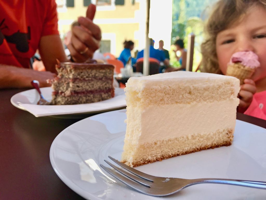 Fetta di torta alla crema su un piatto, con una bambina felice in un ristorante di Villach.