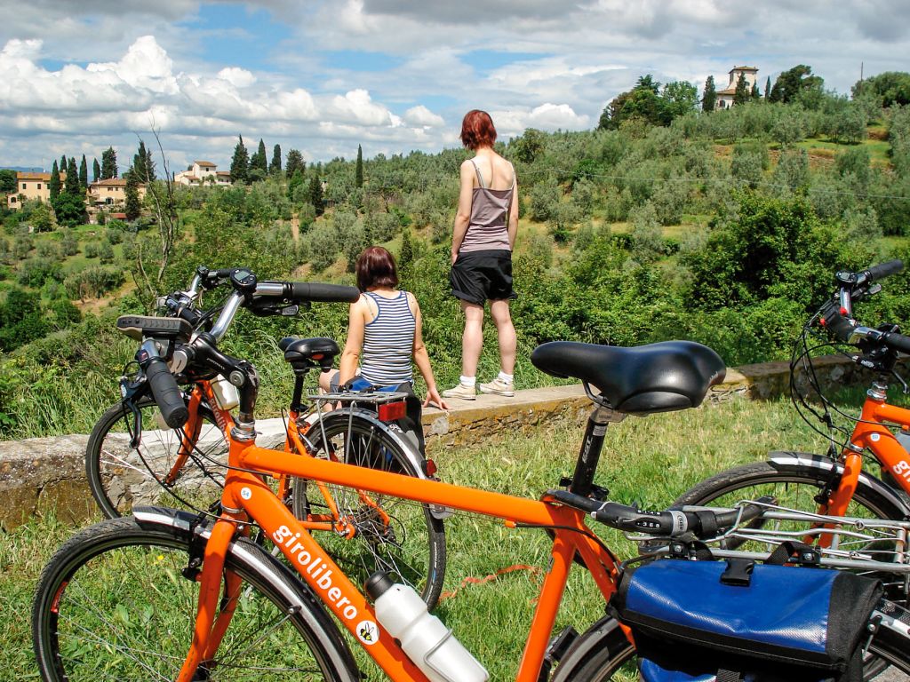 Ciclisti in sosta con biciclette arancioni "Girolibero" parcheggiate vicino a un vigneto in Toscana, Italia.