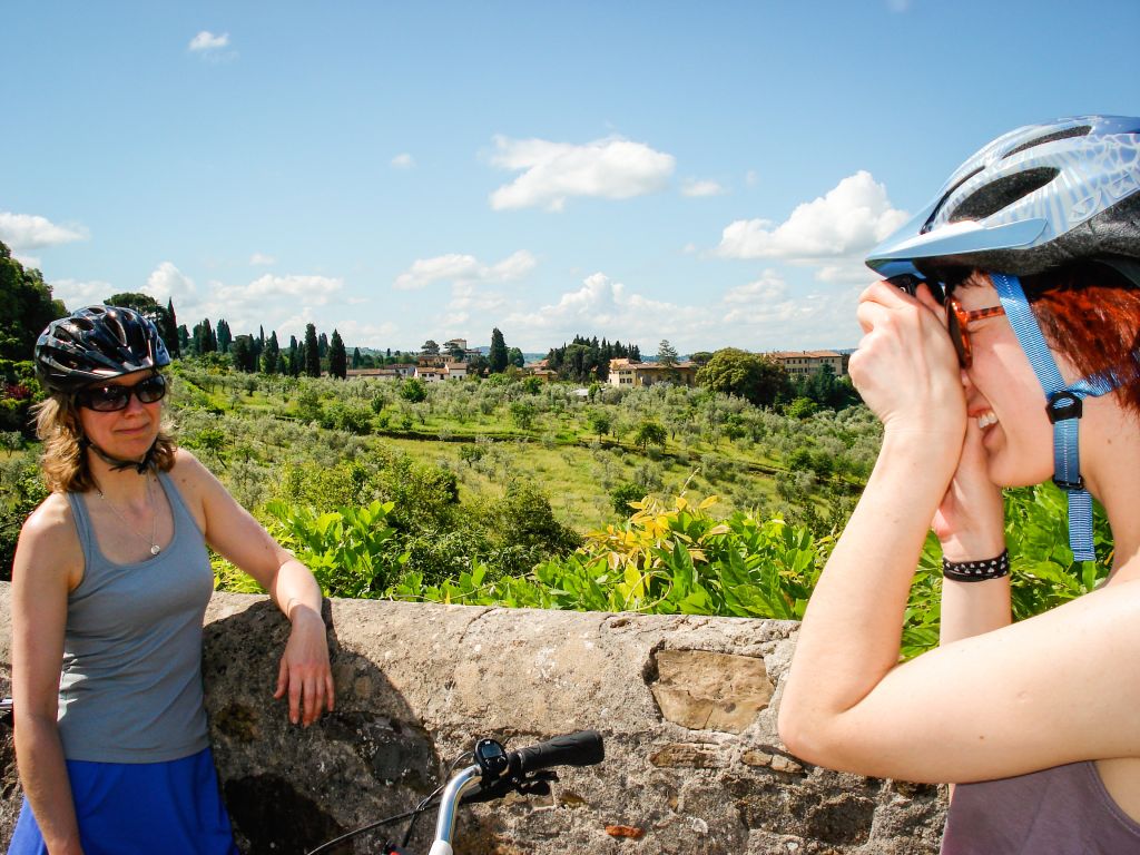 Donna con caschetto e bici in posa per una foto in un paesaggio tipico toscano