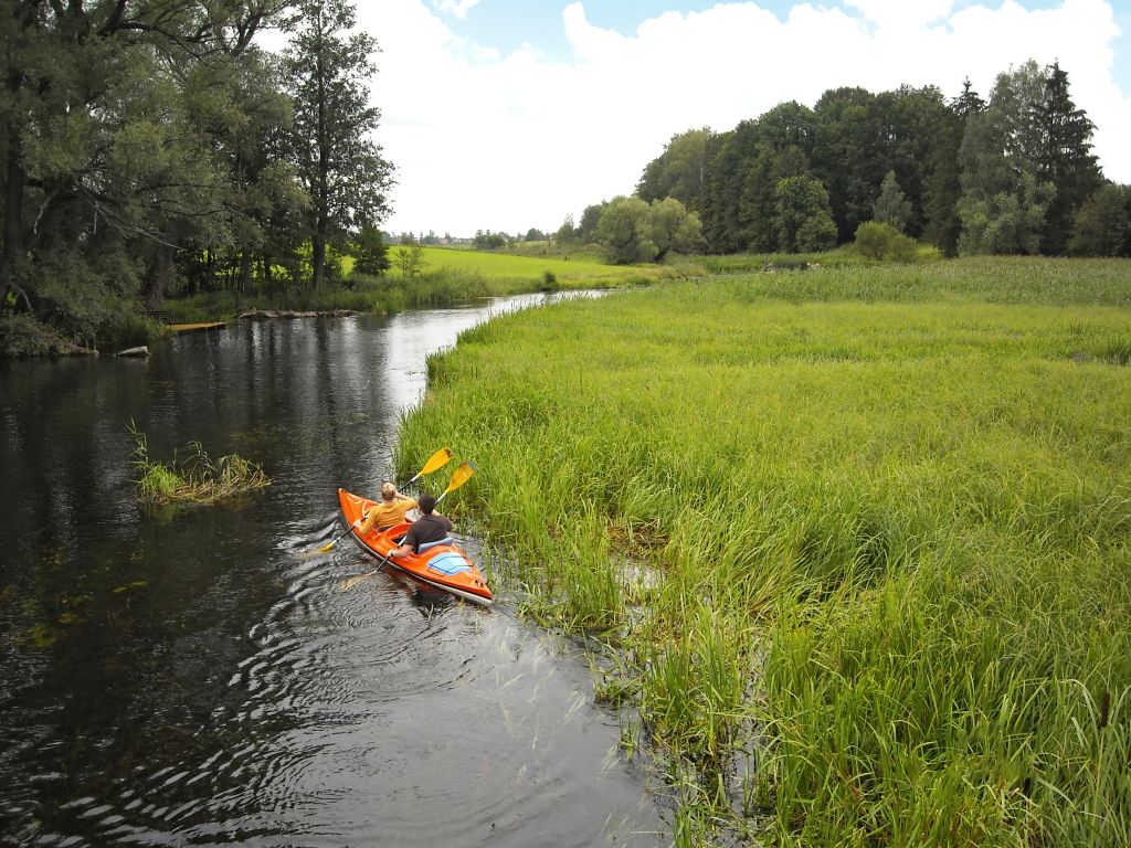 Persone in canoa lungo un fiume circondato da vegetazione nella regione dei Laghi Masuri, Polonia.