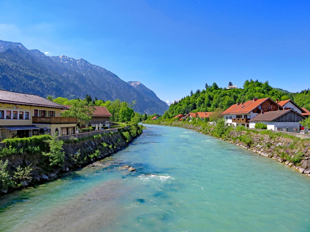 Fiume Isar che attraversa un villaggio alpino in Baviera, Germania, con montagne sullo sfondo.