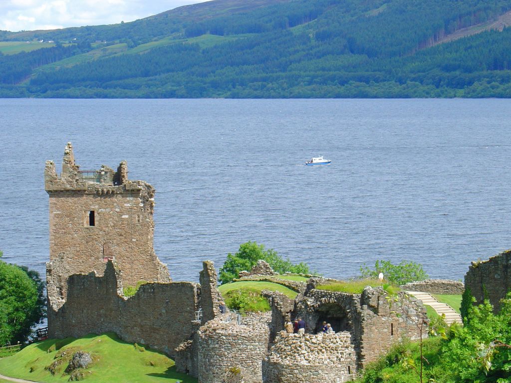 Rovine del castello di Urquhart affacciato sul lago di Loch Ness, con il cielo azzurro e l'acqua calma lungo il Great Glen Way.