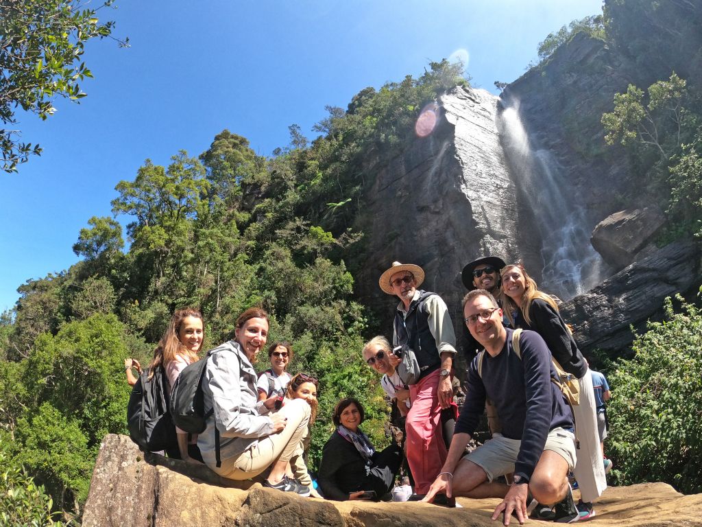 Viaggiatori in escursione davanti a una cascata tropicale nello Sri Lanka, esperienza naturalistica e attiva.