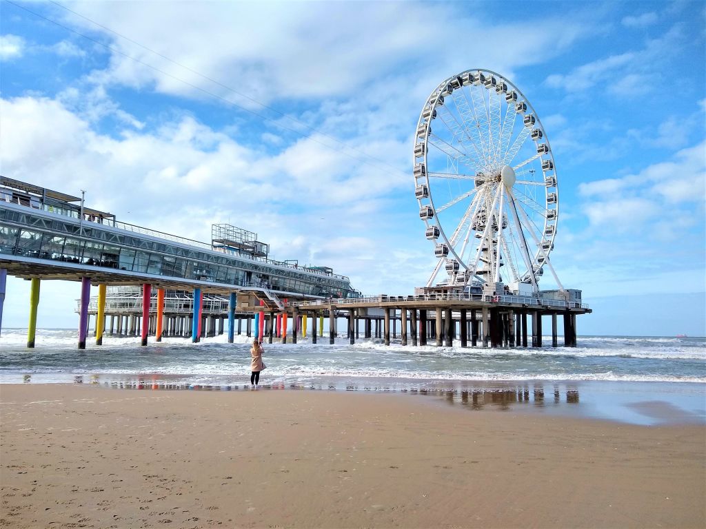 Molo di Scheveningen con la ruota panoramica sul mare e spiaggia sabbiosa nei Paesi Bassi.