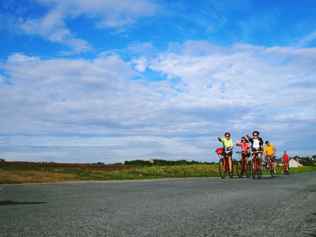 Gruppo di ciclisti che pedala attraverso una strada aperta in Bretagna, sotto un cielo sereno.