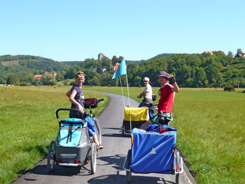 Genitori in bici con carrellino per bambini nei paesaggi verdi della Baviera.