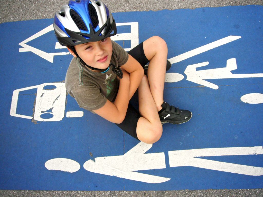 Bambino con casco seduto sulla pista ciclabile con segnaletica orizzontale, Germania.
