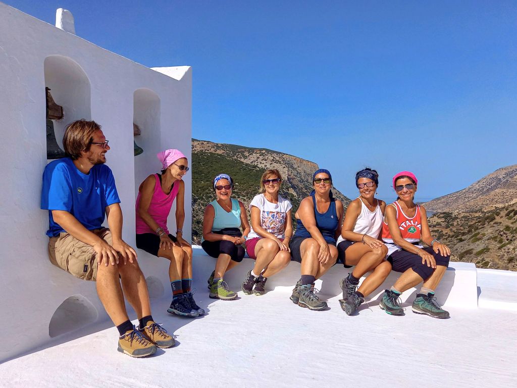 Gruppo di turisti in viaggio con Girolibero seduti sui gradini bianchi di una casa tipica in Grecia, con vista sul mare.