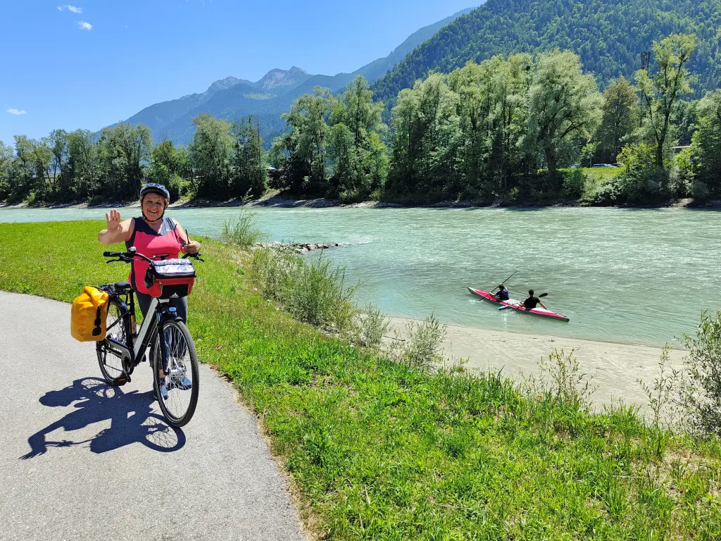 Ciclista lungo la Ciclabile della Drava, con canoisti sul fiume.