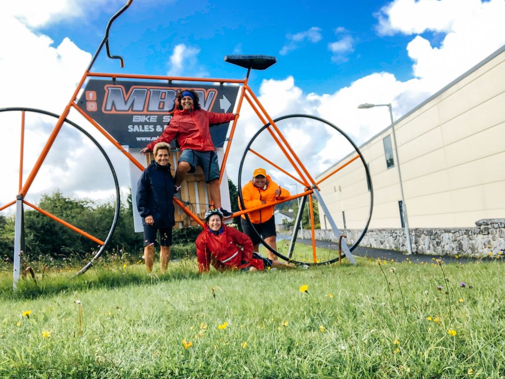 Turisti in viaggio fanno una foto con grande bicicletta decorativa rossa vicino a un edificio, simbolo di benvenuto al Connemara.